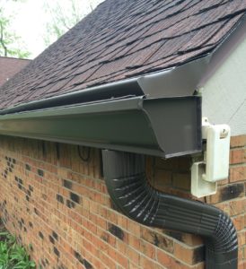 A gutter guard system on black k-style gutters helps prevent clogs on a home with brick siding and a shingle roof.