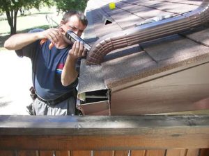 A technician installs a downspout through a covered gutter system.